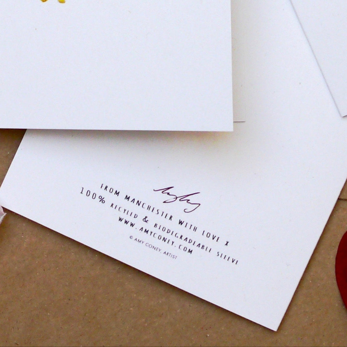 Back of a greeting card with the text 'From Manchester with Love x,' printed on 100% recycled and biodegradable materials. Features the artist's signature and website www.amyconey.com, emphasising sustainability and eco-friendly design.